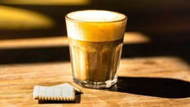 A close-up of a frothy cappuccino and biscuit on a sunlit wooden table, perfect for breakfast themes.