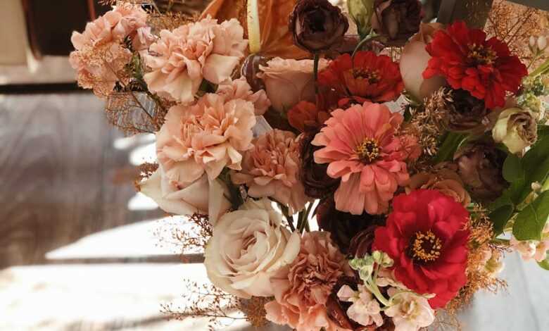 High angle of bunch of fresh red and pink flowers with ribbon placed on wooden floor under table