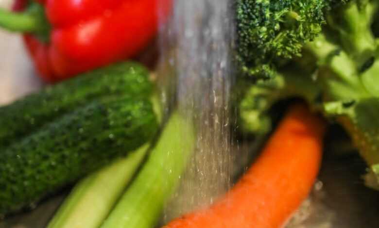 Fresh vegetables under running water in metal bowl