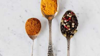 Top view composition with cinnamon and turmeric powder arranged on marble table together with mixed peppercorns used for gourmet and healthy food preparation