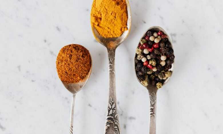 Top view composition with cinnamon and turmeric powder arranged on marble table together with mixed peppercorns used for gourmet and healthy food preparation