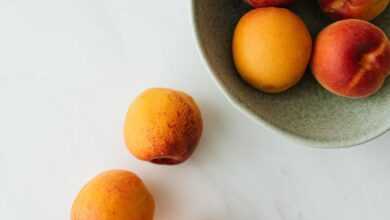 Top view composition of delicious colorful peaches in green ceramic bowl and on white marble table