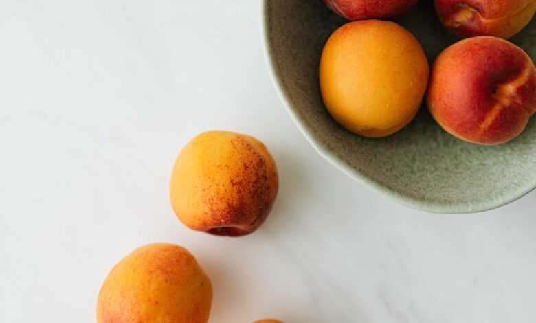 Top view composition of delicious colorful peaches in green ceramic bowl and on white marble table