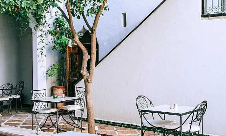 Exterior of modern building and cobblestone yard with decorative pool and tangerine tree over tables with chairs