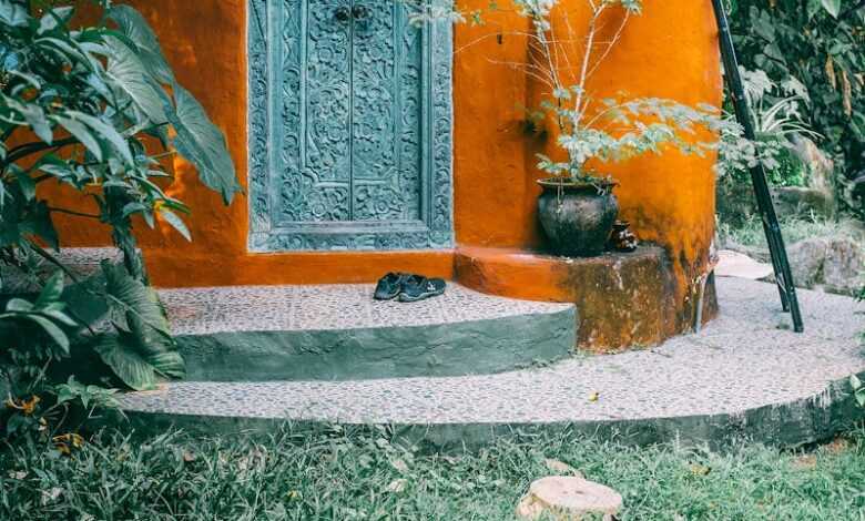 Facade and front door of old stone bright yellow traditional house and green lawn with trees