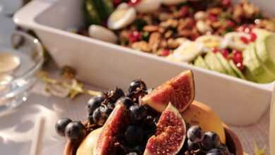 High angle of ceramic plate with fresh fruits and berries on table with various snacks