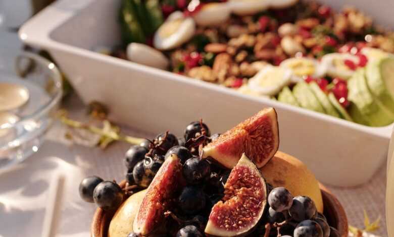 High angle of ceramic plate with fresh fruits and berries on table with various snacks