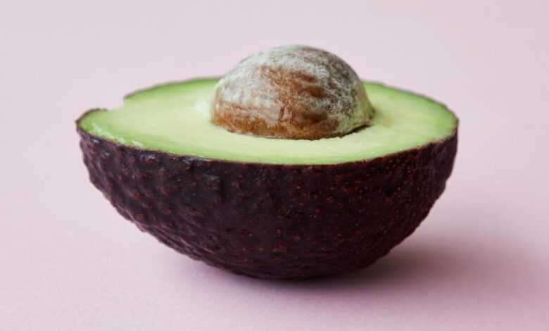 Half of avocado with seed on pink surface