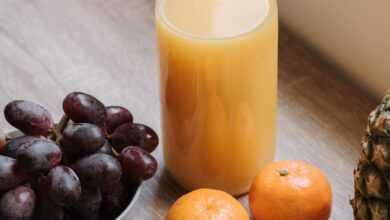 High angle of plastic bottle with juice bowl with red grapes and some mandarins and green apple on table