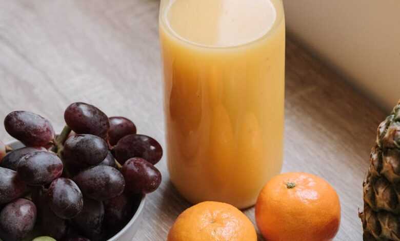 High angle of plastic bottle with juice bowl with red grapes and some mandarins and green apple on table