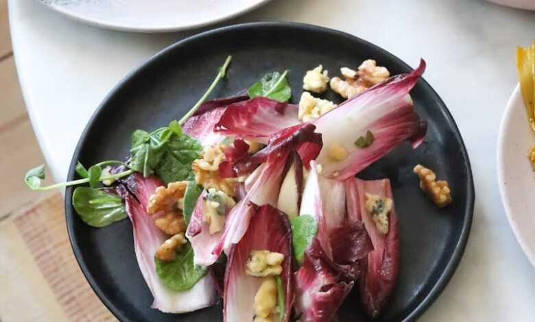 From above of healthy salad with fresh red lettuce and walnuts in plate placed on table with appetizing fish and roasted cauliflower