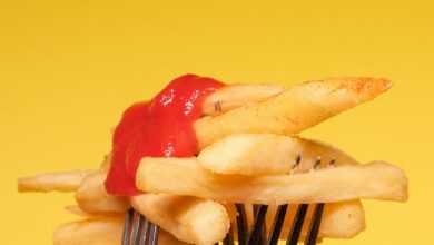 Yummy french fries with ketchup on forks near yellow wall in light studio