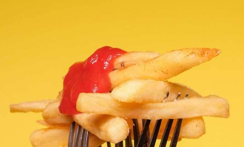 Yummy french fries with ketchup on forks near yellow wall in light studio