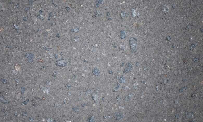 Top view of gray rough textured asphalt with stone inclusions scattered on surface