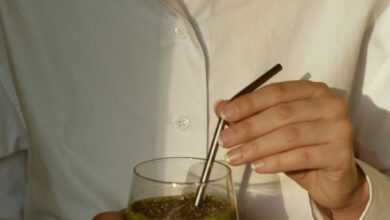 person in white button up shirt holding clear drinking glass with green liquid