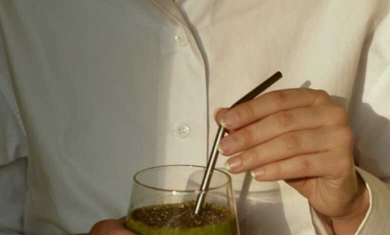 person in white button up shirt holding clear drinking glass with green liquid