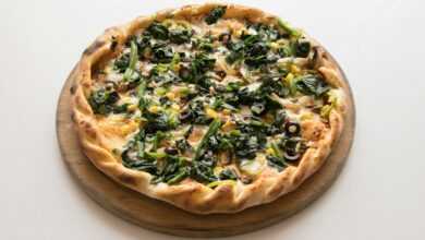 pizza with green leaves and cheese on brown wooden round plate