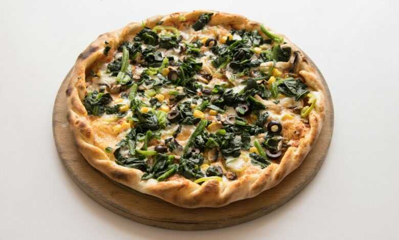 pizza with green leaves and cheese on brown wooden round plate