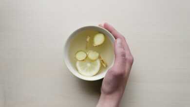 person holding white bowl with sliced lime and ginger inside