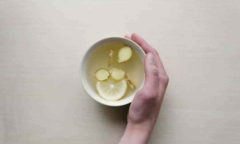 person holding white bowl with sliced lime and ginger inside