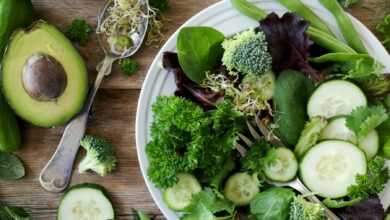 sliced broccoli and cucumber on plate with gray stainless steel fork near green bell pepper, snowpea, and avocado fruit