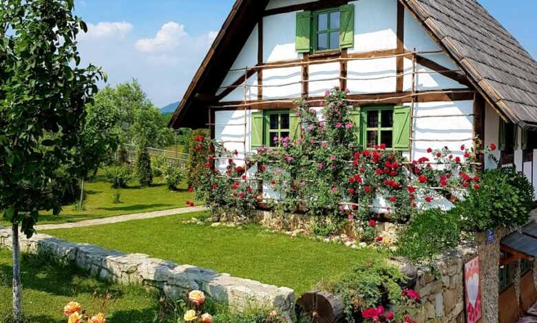 brown wooden house surrounded by green trees and flowers under blue sky during daytime