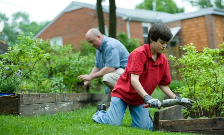 man in red polo shirt and blue denim jeans sitting on brown wooden bench during daytime