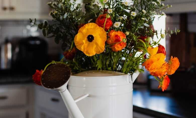 a white watering can filled with flowers on a kitchen counter